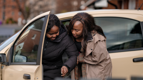 A person is getting helped out of the car by their carer