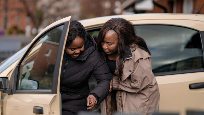 A person is getting helped out of the car by their carer