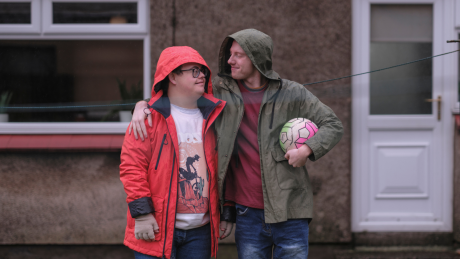Two people standing outside a house sharing a hug with one holding a football under his arm