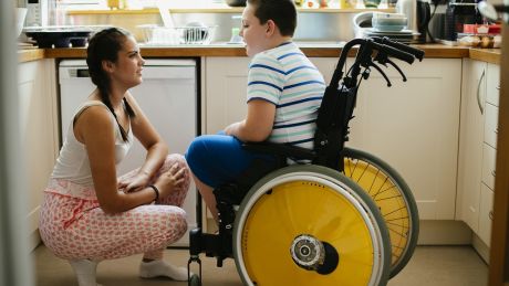 Boy in wheelchair in a kitchen with a woman crouching in front of him talking